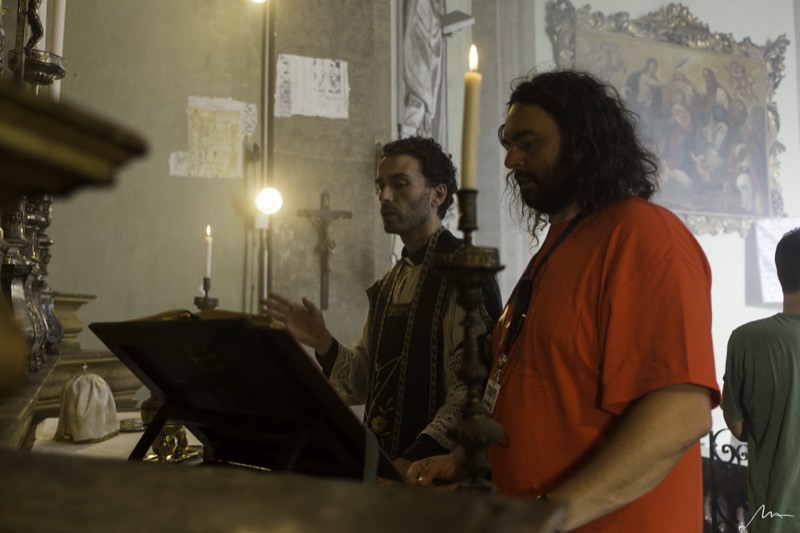 Gianni Aureli dirige un attore in costume dentro una chiesa, sul set di Aquile Randagie