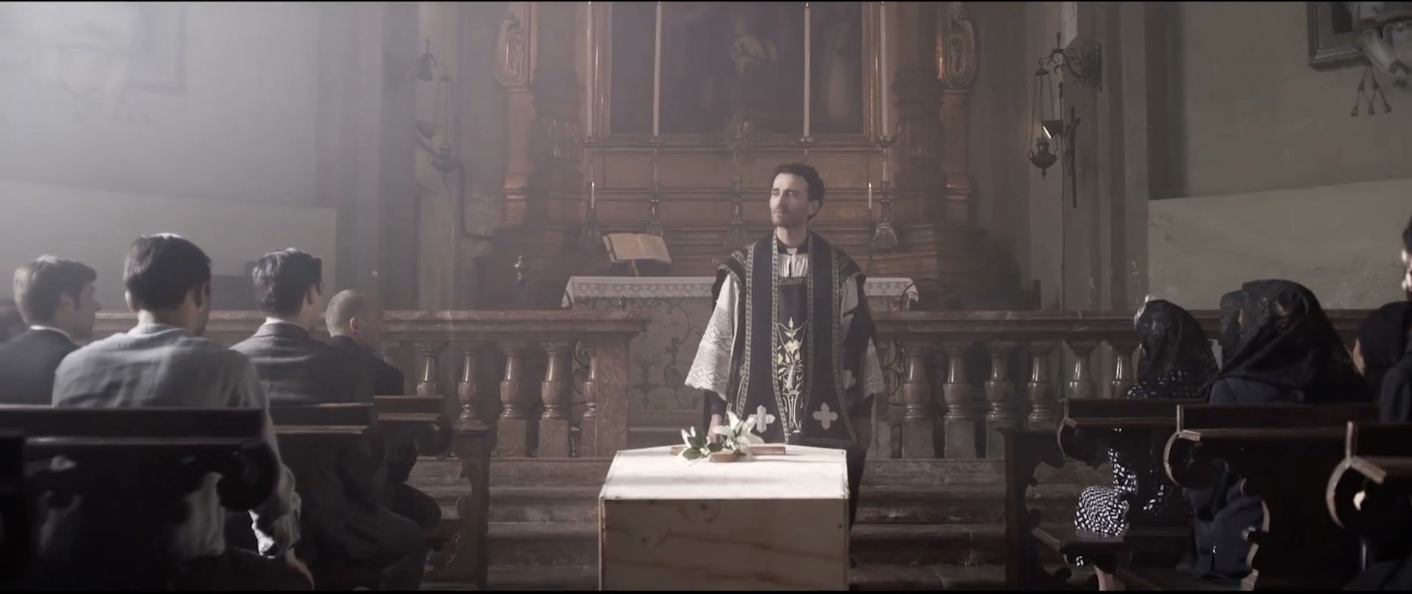 Fotogramma: un funerale in chiesa, la bara al centro e il sacerdote all'altare