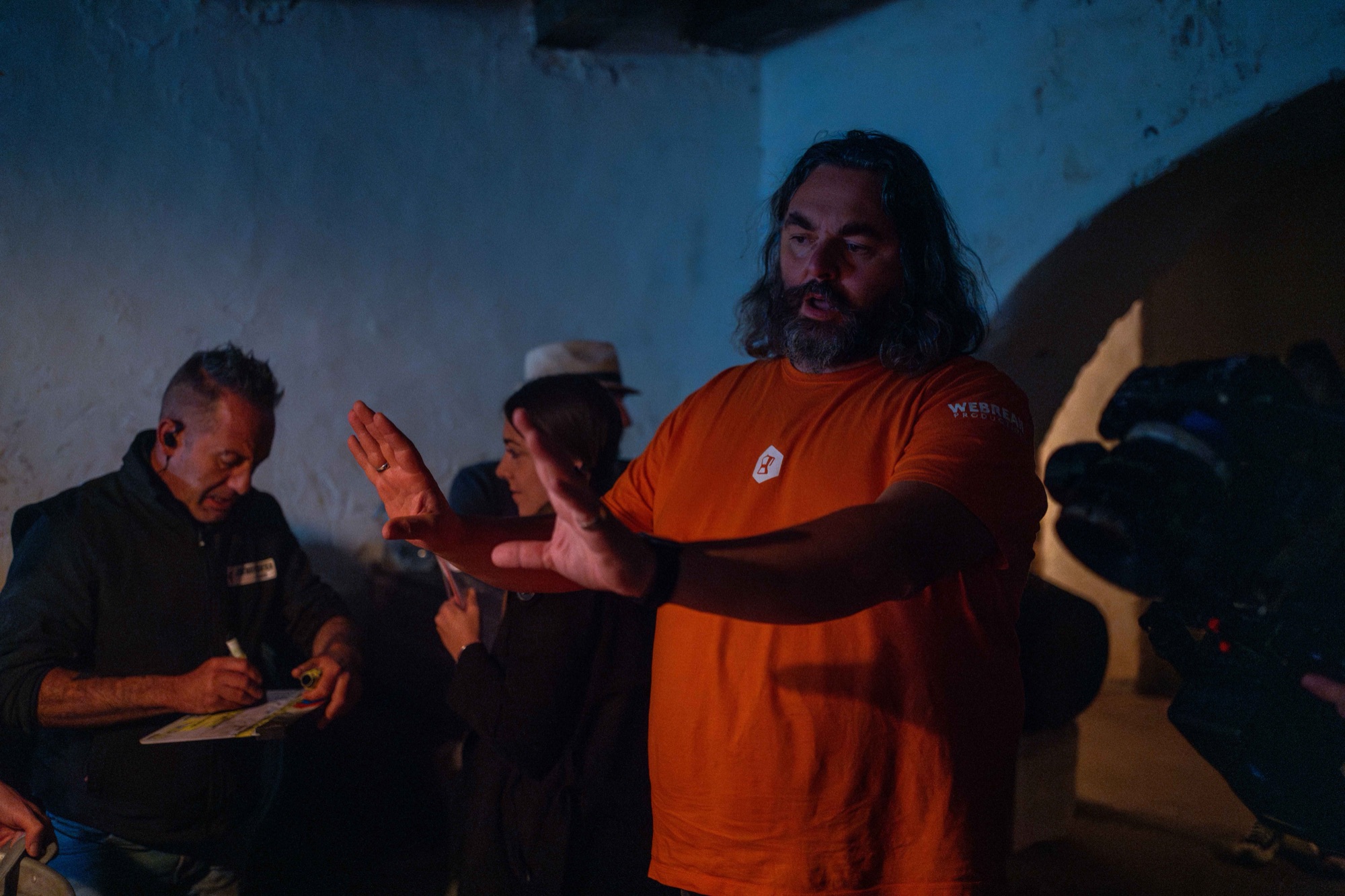 Gianni Aureli spiega una scena con le mani, sul set de La Terza Volta, in una cantina illuminata di blu