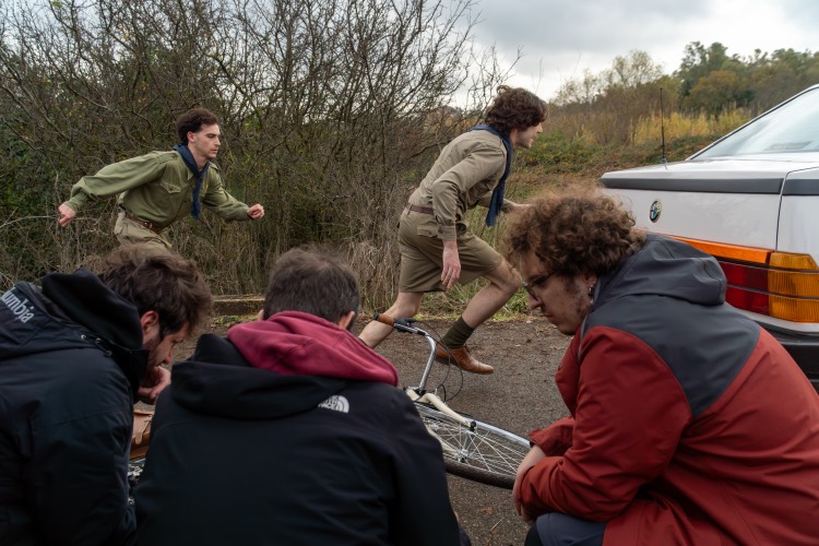 Due ragazzi in divisa scout corrono lungo una strada di campagna, la troupe li riprende in primo piano